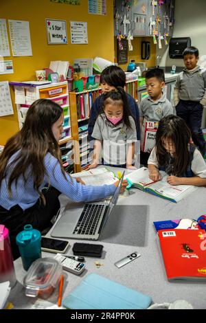 Junge multiethnische Schüler stellen sich für Ratschläge in Arbeitsbüchern ihres Grundschullehrers an einer katholischen Grundschule in Südkalifornien auf. Stockfoto