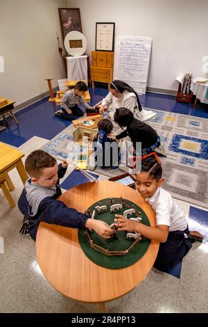 Eine hispanische Nonne hilft einem Jungen mit Kunstarbeit, während andere Jungen mit Spielzeugschafen spielen und Mädchen mit einem Puppenhaus in einem katholischen Eleme in Südkalifornien spielen Stockfoto