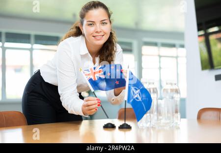 Die Sekretärin setzt die Flaggen der NATO (OTAN) und Australiens auf den Tisch, bevor Verhandlungen mit hochrangigen politischen Persönlichkeiten geführt werden Stockfoto