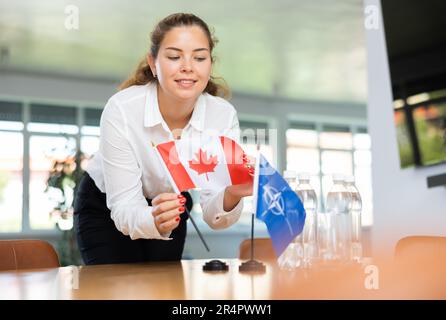 Die Sekretärin setzt die Flaggen der NATO (OTAN) und Kanadas auf den Tisch, bevor Verhandlungen mit hochrangigen politischen Persönlichkeiten geführt werden Stockfoto