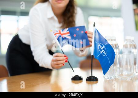 Die Sekretärin setzt die Flaggen der NATO (OTAN) und Australiens auf den Tisch, bevor Verhandlungen mit hochrangigen politischen Persönlichkeiten geführt werden Stockfoto