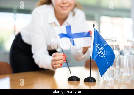 Die Sekretärin setzt die Flaggen der NATO (OTAN) und Finnlands auf den Tisch, bevor die Verhandlungen mit hochrangigen politischen Persönlichkeiten beginnen Stockfoto