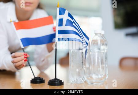 Ein nicht wiedererkennbares Mädchen setzt vor internationalen Verhandlungen Zwergflaggen von Griechenland und den Niederlanden Stockfoto