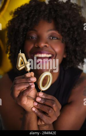 Afrikanische Frau lächelt auf ihrer 40. Geburtstagsparty mit 40 goldenen Kerzen. Stockfoto