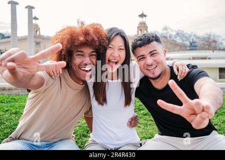 Eine Gruppe von Freunden, die das Friedenszeichen gestalten, in die Kamera schauen und zusammen lächeln. Drei multirassische Teenager, die Spaß haben, den Siegesfingern zu zeigen. Positive, fröhliche Schüler, die lachen. Hochwertiges Foto Stockfoto