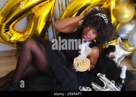 Afrikanische Frau mit Champagnerglas und Kuchen, feiert ihren 40. Geburtstag auf einer Party. Stockfoto