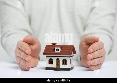 Heimsicherheitskonzept. Mann mit Hausmodell am weißen Tisch, Nahaufnahme Stockfoto