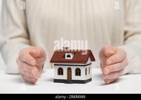 Heimsicherheitskonzept. Frau mit Hausmodell am weißen Tisch, Nahaufnahme Stockfoto