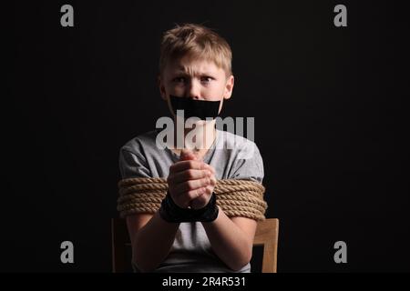 Ein kleiner Junge mit gefesseltem Mund, der vor dunklem Hintergrund als Geisel genommen wurde Stockfoto