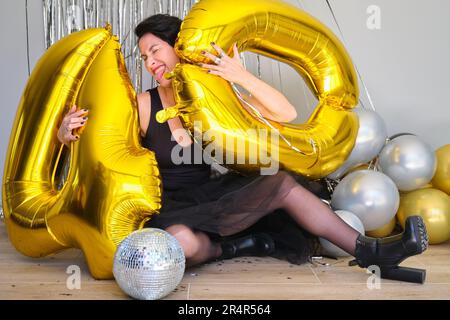 Weiße Frau auf einer 40. Geburtstagsparty mit 40 goldenen Ballons zum Geburtstag auf dem Boden. Stockfoto