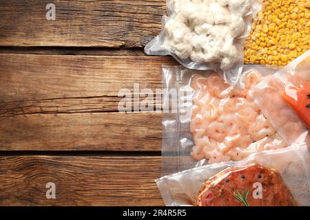 Leckeres Essen in Vakuumverpackungen auf Holztisch, flach liegend. Platz für Text Stockfoto