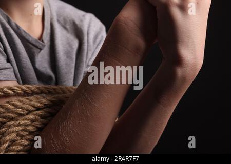 Ein kleiner Junge gefesselt und als Geisel genommen, auf dunklem Hintergrund, Nahaufnahme Stockfoto