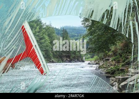 Frau putzt Fenster mit Abzieher, schließt. Blick durch klares Glas auf den malerischen Bergfluss Stockfoto