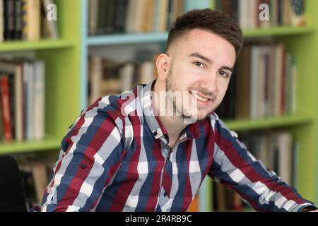 Handsome man Sitting in the Library - Schüler, der die Prüfung vorbereitet und Unterricht in der Schulbibliothek nimmt Stockfoto
