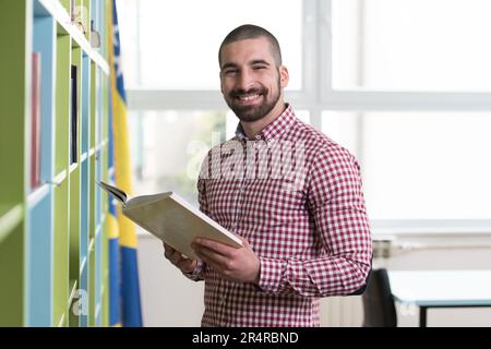Handsome man Standing in the Library - Schüler, der die Prüfung vorbereitet und Unterricht in der Schulbibliothek nimmt Stockfoto