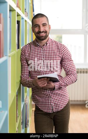 Handsome man Standing in the Library - Schüler, der die Prüfung vorbereitet und Unterricht in der Schulbibliothek nimmt Stockfoto