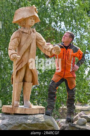 Heinersdorf, Deutschland. 23. Mai 2023. Christian Mücke, Kettensägenkünstler, steht neben der lebensgroßen Holzfigur des preußischen Königs Friedrich II., die er erschaffen hat. Speedcarving ist der Name, der der Motorsägenkunst gegeben wird, in der Skulpturen aus Baumstämmen in einer bestimmten Zeit erstellt werden. Und es scheint immer mehr Anhänger zu gewinnen. Seit zehn Jahren treten die Besten bei den deutschen Meisterschaften an. Eine Qualifikationsrunde findet jetzt in Brandenburg statt. (An dpa-Korr: 'Schnell und geschickt mit scharfer Säge') Kredit: Patrick Pleul/dpa/Alamy Live News Stockfoto