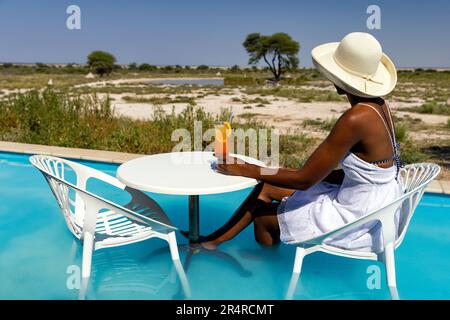 Eine Frau, die einen Drink im Planschbecken in Onguma The Fort, Onguma Game Reserve, Namibia, Afrika genießt Stockfoto