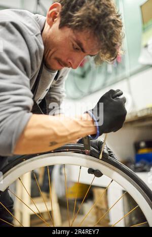 Hispanischer Fahrradmechaniker, der in einer Werkstatt Schutzhandschuhe verwendet, um einen Airless-Reifen von einem Rad zu entfernen. Selektive Fokuskomposition. Kopierbereich Stockfoto