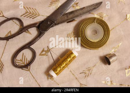 Rolle mit goldenem Faden und Schere mit Kaugummi auf metallischem Chiffon-Stoff Stockfoto