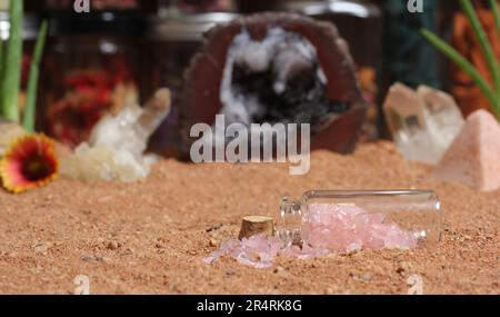 Flasche Rosenquartz Chakra Stones auf rotem Sand mit Geode Rock im Hintergrund Stockfoto