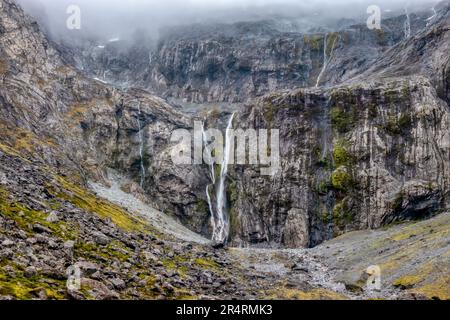 Wasserfälle, Nebel und Regen über einer steilen Granitwand auf der Südinsel Neuseelands, in der Nähe des Eingangs zum Homer Tunnel in der Nähe des Milford Sound. Stockfoto