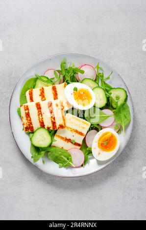 Gesundes Ketogenic Paleo Gericht, gegrilltes Halloumi mit Salat, Rettich, Gurke, und gekochtes Ei auf hellem Hintergrund, Detox, Diet Lunch Stockfoto