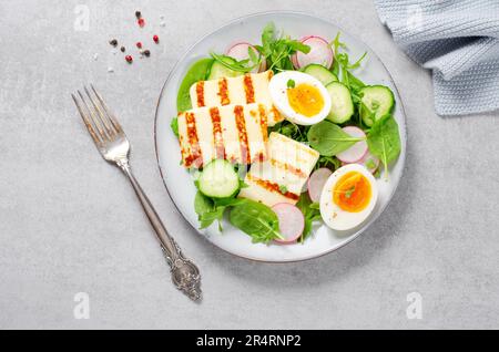 Gesundes Ketogenic Paleo Gericht, gegrilltes Halloumi mit Salat, Rettich, Gurke, und gekochtes Ei auf hellem Hintergrund, Detox, Diet Lunch Stockfoto