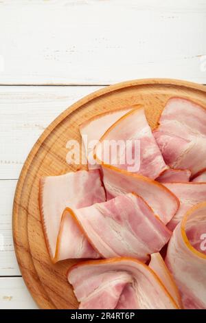 Frischer kaltgeschnittener Speck auf dem Holzschneidbrett auf weißem Hintergrund. Draufsicht. Stockfoto