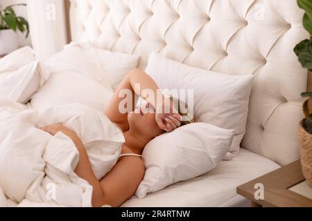 Eine junge weiße Frau in Übergröße mit Hand auf den Augen schläft bequem auf einem gemütlichen Bett zu Hause Stockfoto