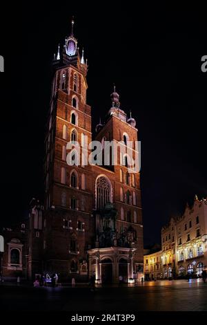 Vertikales Nachtfoto des zentralen Platzes Rynok Glavny mit St. Marienkirche in Krakau, Polen Stockfoto