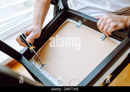 Ein Mann mittleren Alters, der zu Hause einen Stuhl repariert Stockfoto