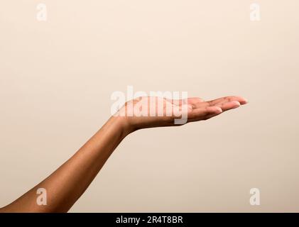 Eine anonyme afroamerikanische Frau, die mit Handfläche Leerraum für Werbung vor beigefarbenem Hintergrund demonstriert Stockfoto