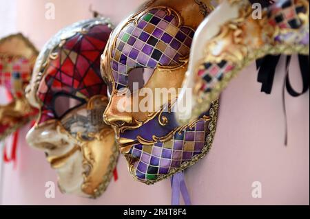 Profilansicht der traditionellen venezianischen Masken für den Karneval, die in Reihe an der rosafarbenen Wand in Venedig, Italien, hängen. Stockfoto