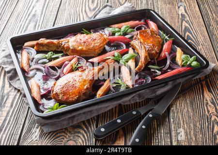 Hausgemachte Schweinekoteletts mit roten Zwiebeln, Kräutern und Rhabarber in Nahaufnahme auf einem Backblech auf dem Tisch. Horizontal Stockfoto