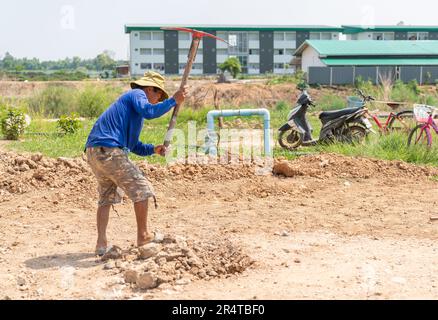 Die Arbeiter verwenden eine Spitzhacke, um die Bodenoberfläche vor dem Gießen von Beton zu ebnen. Stockfoto