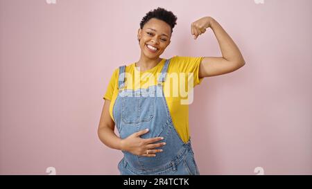 Junge schwangere Frau, die selbstbewusst lächelt und eine starke Geste auf isoliertem pinkfarbenen Hintergrund macht Stockfoto