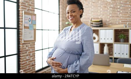 Junge Schwangere Geschäftsarbeiterin lächelt selbstbewusst und berührt den Bauch im Büro Stockfoto