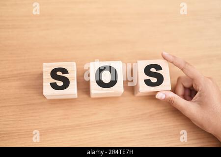 Frauenhand hält Würfel mit sos-Wort auf dem Tisch Stockfoto