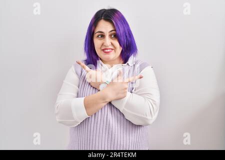 Große Frau mit lila Haaren, die auf weißem Hintergrund steht und mit den Fingern auf beide Seiten zeigt, unterschiedliche Richtungen Stockfoto