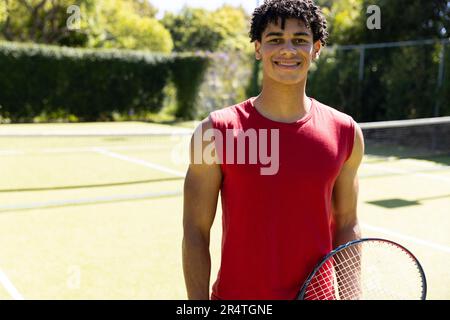 Porträt eines lächelnden, birassischen jungen Mannes, der im Gericht Tennisschläger hält Stockfoto