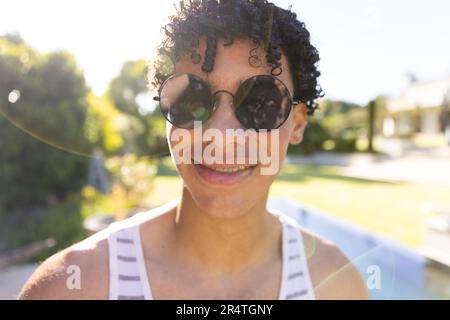 Nahaufnahme eines lächelnden, birassischen jungen Mannes, der eine Sonnenbrille trägt und im Hof posiert Stockfoto