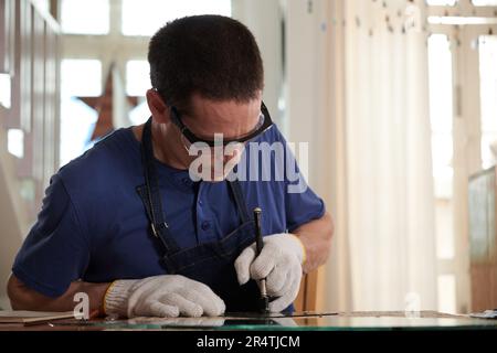 Konzentrierter Handwerker in Schutzbrillen und Textilhandschuhen, Schneidspiegel für Kunden Stockfoto