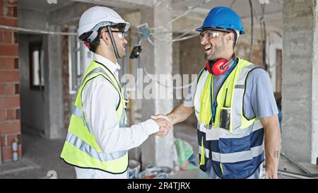 Zwei selbstbewusste Bauarbeiter schütteln sich auf der Baustelle die Hand Stockfoto