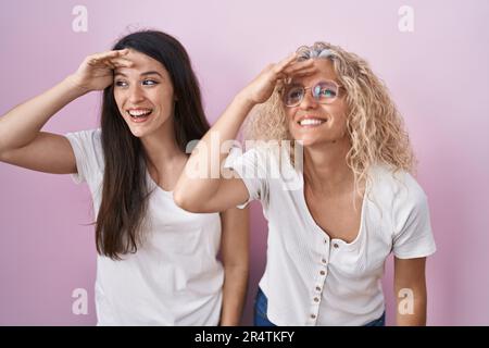 Mutter und Tochter standen zusammen auf rosa Hintergrund, sehr glücklich und lächelnd, mit Hand über Kopf. Suchbegriff. Stockfoto