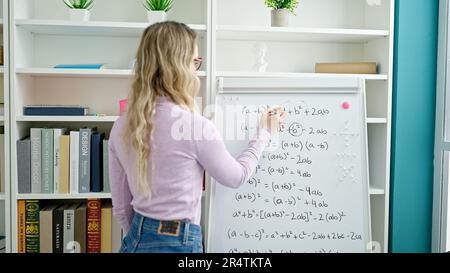 Junge blonde Lehrerin, die Mathematik unterrichtet, schreibt auf einem Whiteboard im Klassenzimmer Stockfoto