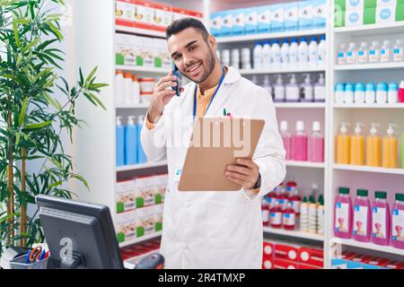 Junger hispanischer Apotheker, der mit dem Smartphone spricht und in der Apotheke Dokumente liest Stockfoto
