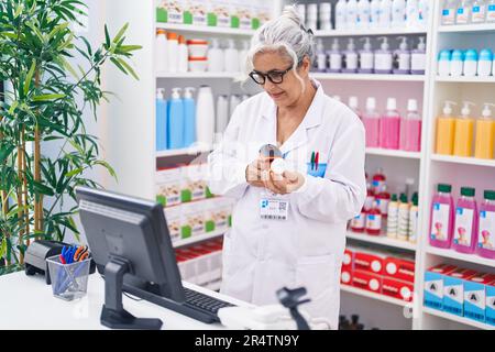 Grauhaarige Frau im mittleren Alter, Apothekerin, die in der Apotheke eine Tablettenflasche scannt Stockfoto
