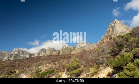 Wolken über der 12 Apostles Mountain Range, auf dem Tafelberg, Kapstadt, mit Pflanzen, die durch wilde Brände im Vordergrund beschädigt wurden. Stockfoto