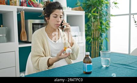 Junge schwangere Frau, die eine medizinische Beratung durch Smartphone mit Pillen im Speisesaal Stockfoto